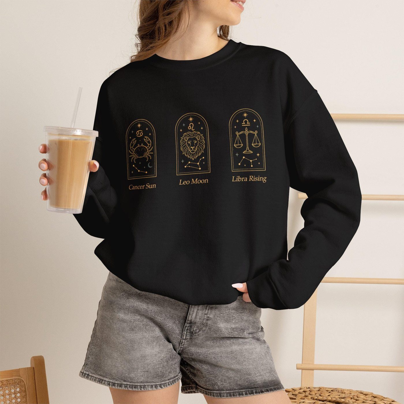 Person wearing a black crewneck sweatshirt with three small gold zodiac arches across the chest